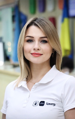 Жінка з довгим світлим волоссям, у білій футболці з логотипом. Світла шкіра, виразний макіяж.